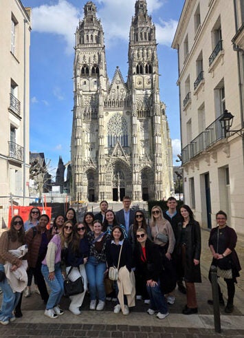 A group of people pose in front of a gothic-style church. The church is several hundred yards behind them. 