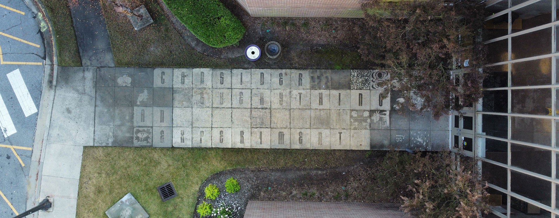 A bird’s eye view from high off the ground reveals street art created by East Carolina University students with the words “Consider everything an experiment,” which is surrounded by student designs on a sidewalk. 