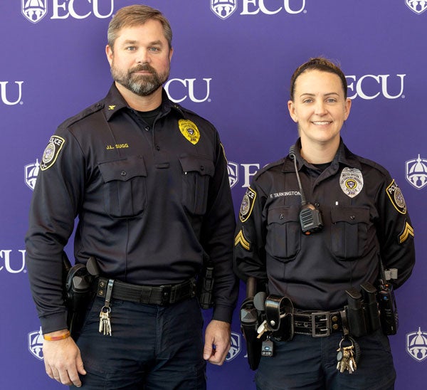     A man in a police uniform stands next to a short woman in a police uniform. 