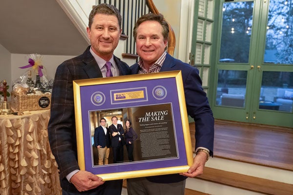 Two men in suits hold a plaque.