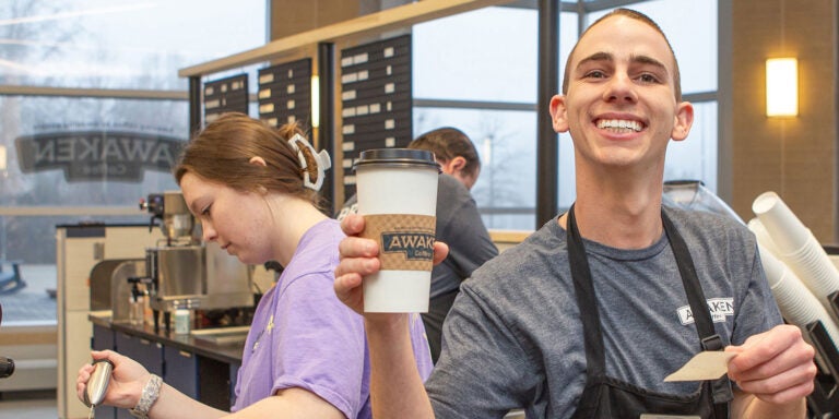 A man in a gray shirt and black apron holds a coffee order.