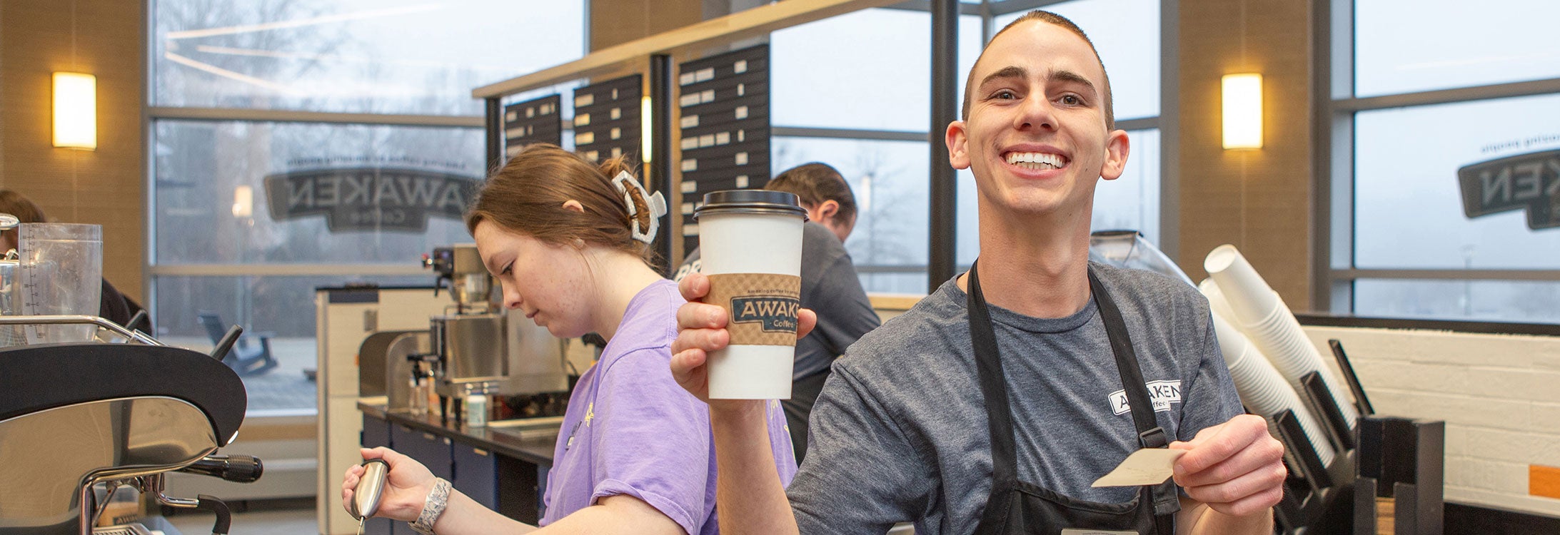 A man in a gray shirt and black apron holds a coffee order.