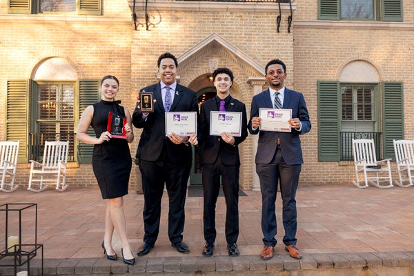 A young woman and three young men stand on steps. The young woman is holding a trophy while the young men hold certificates. 