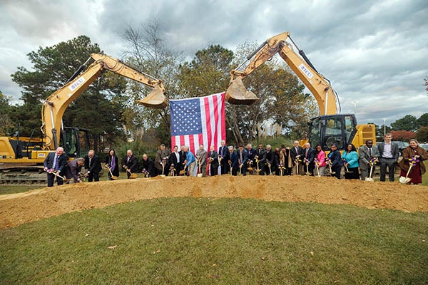 : A group of more than twenty people dressed in business professional attire break ground with gold shovels at the sight of the new ECU Center for Medical Education Building.