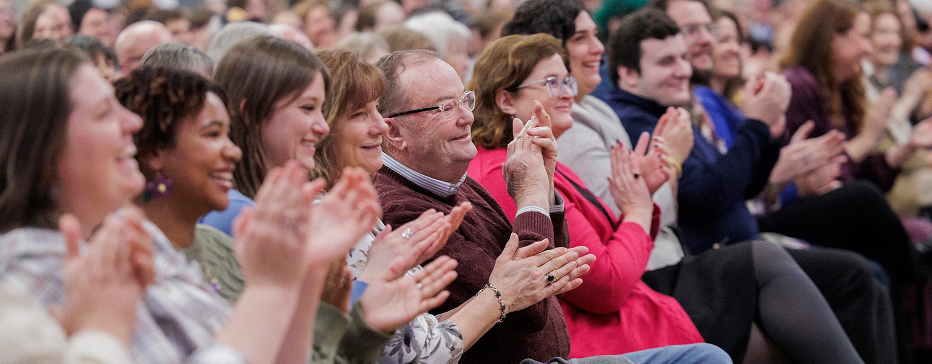 Alt Text: A group of audience members sit smiling and clapping as they welcome a man to East Carolina University’s Main Campus Student Center.